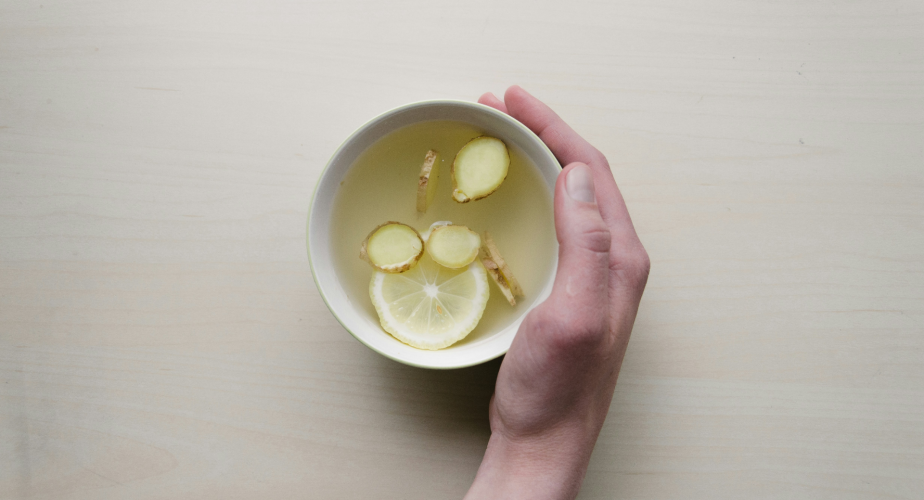 hand holding a mug of ginger and lemon tea on a table