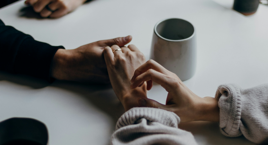 man and women holding hands on table with mug