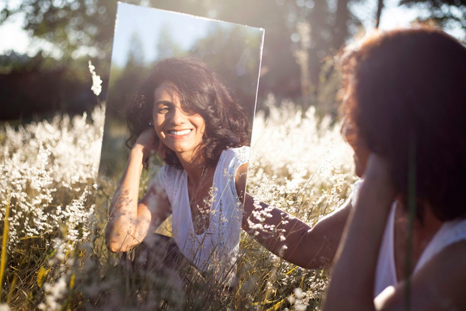 Woman looking in a mirror in the sunlight in a field