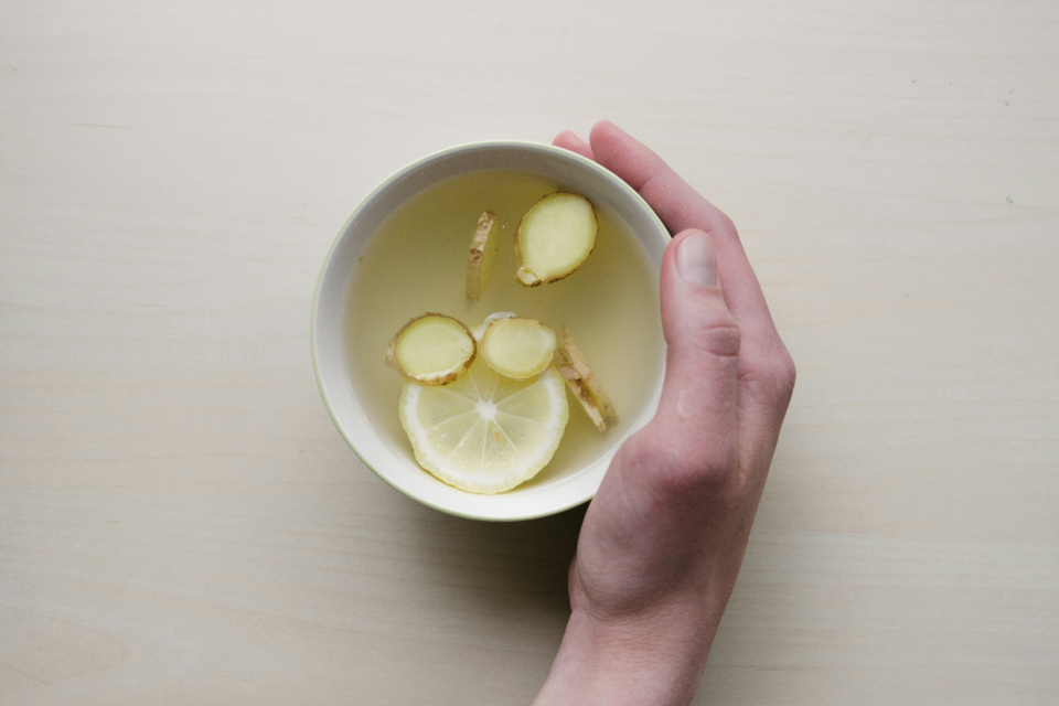 hand holding a mug of ginger and lemon tea on a table