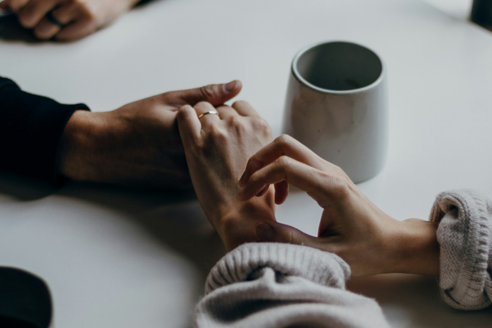 man and women holding hands on table with mug